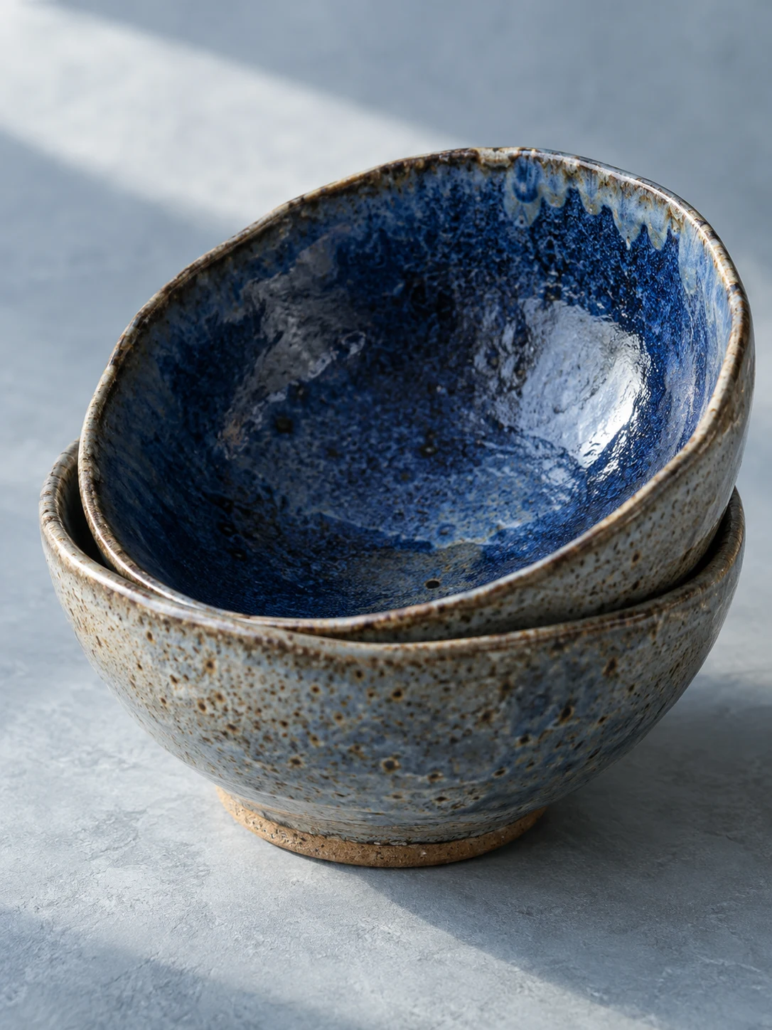 A close study of the pooled cobalt glaze and speckled clay rims of two nested bowls.